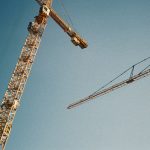 Two construction cranes against a clear blue sky